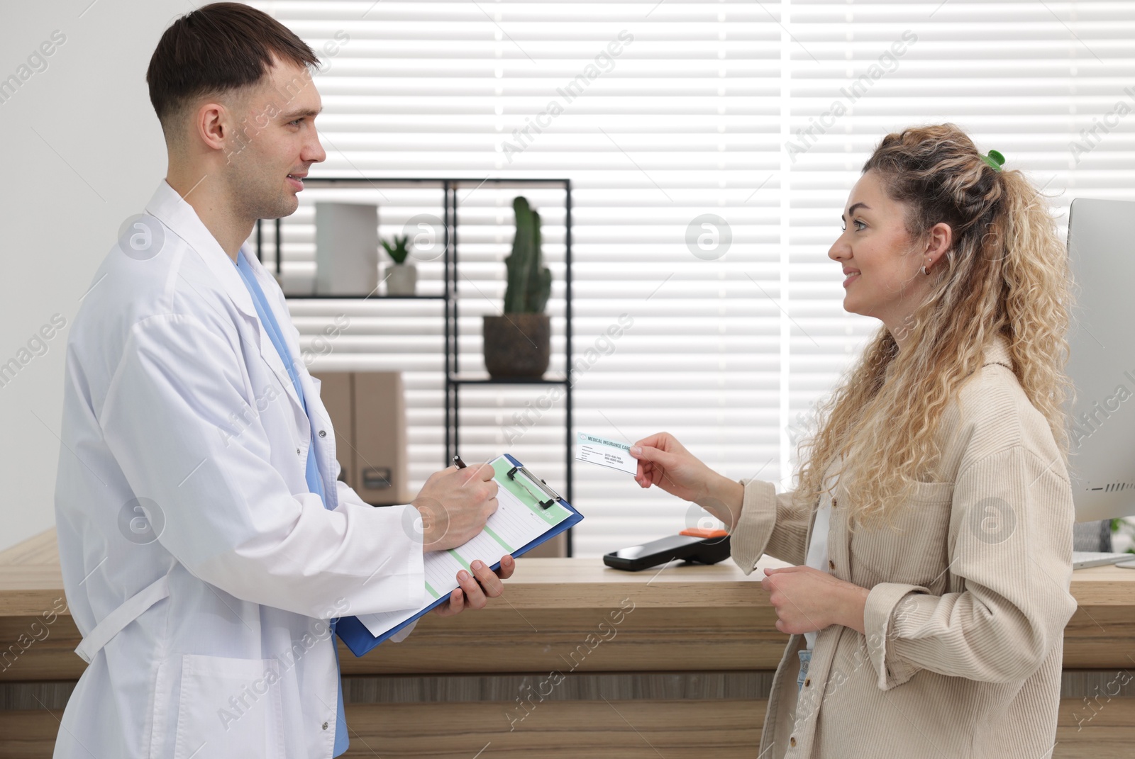 Photo of Smiling patient with medical insurance card and receptionist filling document in clinic