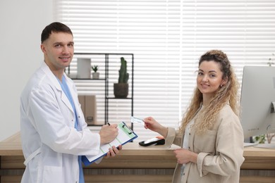 Smiling patient with medical insurance card and receptionist filling document in clinic