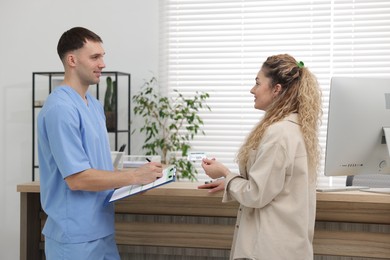 Photo of Smiling patient with medical insurance card and receptionist filling document in clinic