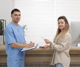 Smiling patient with medical insurance card and receptionist filling document in clinic