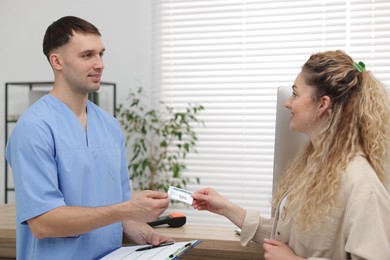 Photo of Smiling patient giving medical insurance card to receptionist in clinic