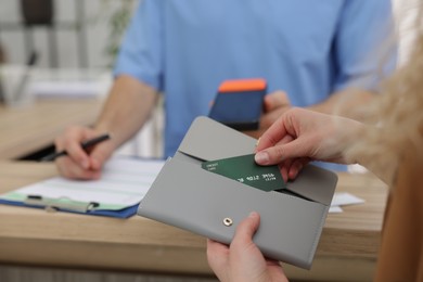 Photo of Patient taking credit card out of wallet and receptionist with terminal at counter, selective focus