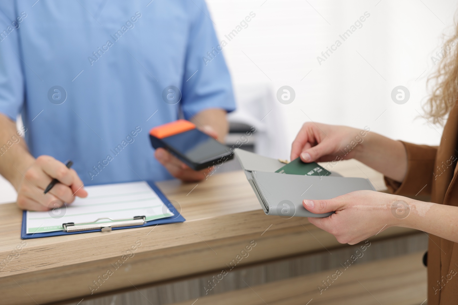 Photo of Patient taking credit card out of wallet and receptionist with terminal at counter, selective focus