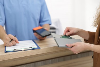 Patient taking credit card out of wallet and receptionist with terminal at counter, selective focus