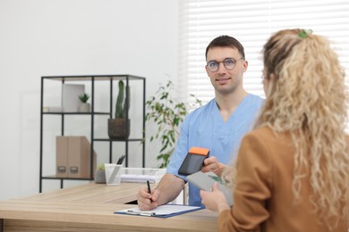 Photo of Patient taking credit card out of wallet and smiling receptionist with terminal at counter in clinic. Space for text