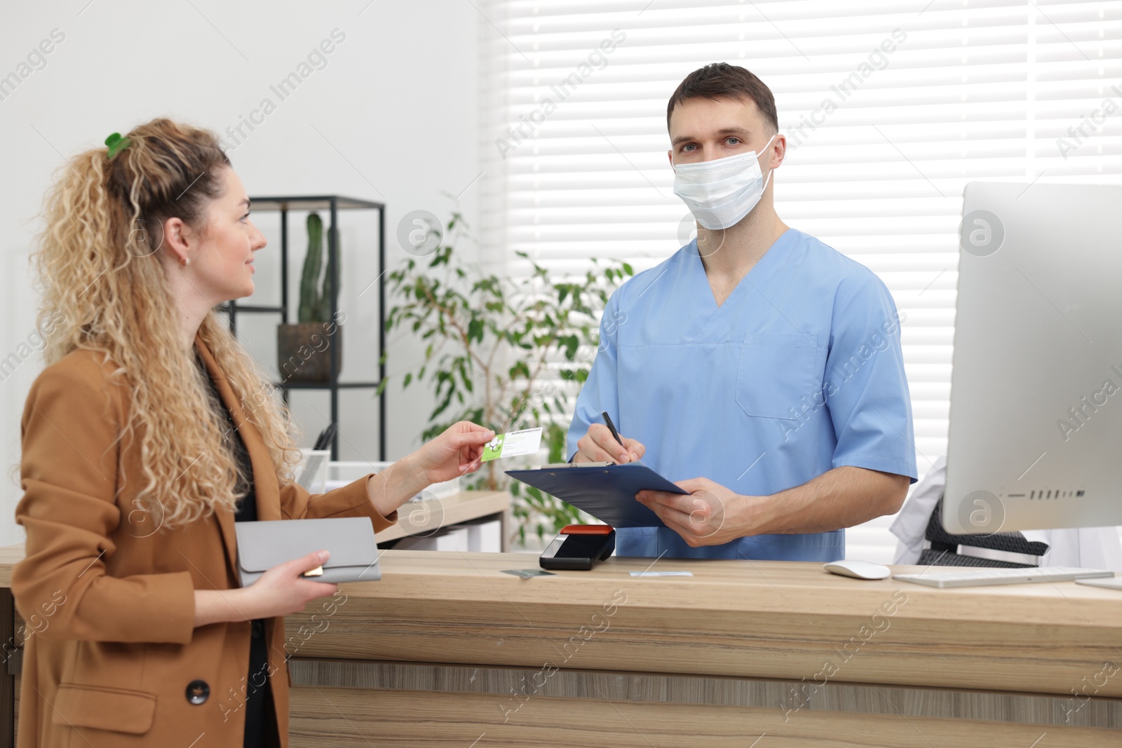 Photo of Patient with medical insurance card and receptionist filling document at counter in clinic