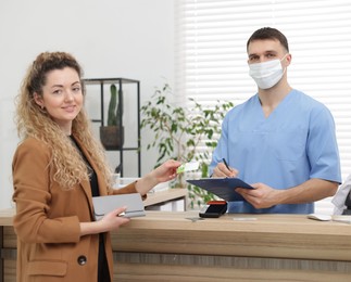 Smiling patient with medical insurance card and receptionist filling document at counter in clinic