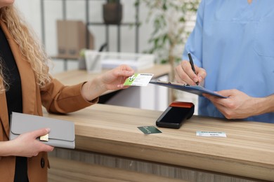 Patient with medical insurance card and receptionist filling document at counter in clinic, closeup