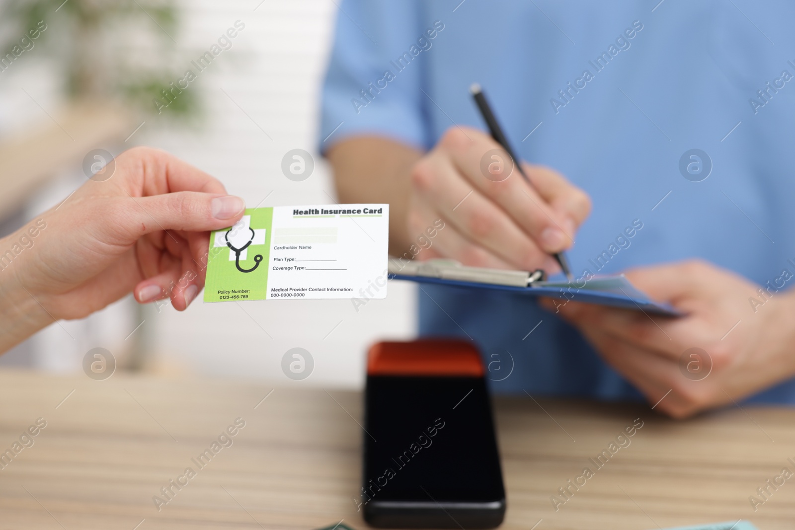 Photo of Patient with medical insurance card and receptionist filling document at counter in clinic, selective focus