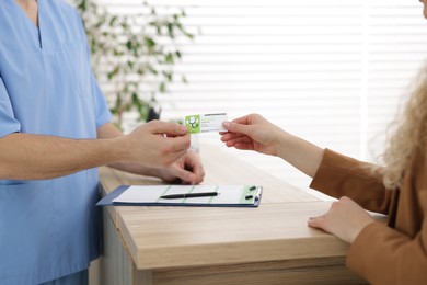 Photo of Patient giving medical insurance card to receptionist at wooden counter in clinic, closeup