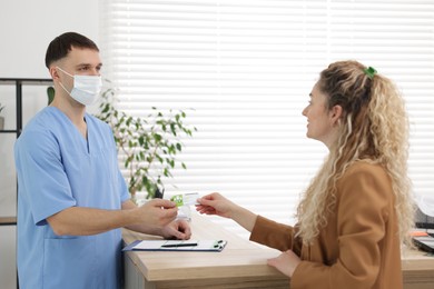 Photo of Patient giving medical insurance card to receptionist in clinic