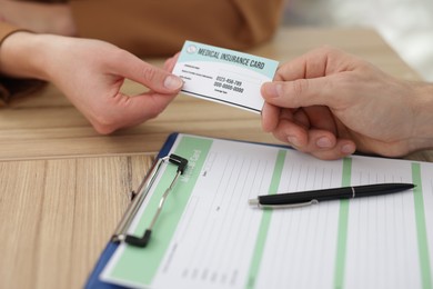 Photo of Patient giving medical insurance card to receptionist at wooden counter in clinic, closeup