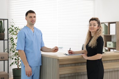 Smiling patient filling document and receptionist with medical insurance card at counter in clinic