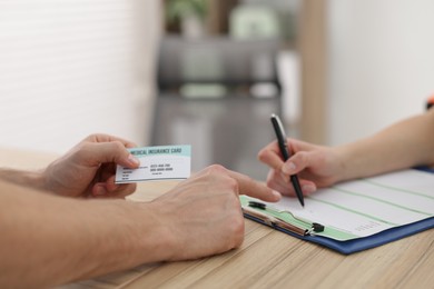 Photo of Patient filling document and receptionist with medical insurance card at wooden counter in clinic, closeup