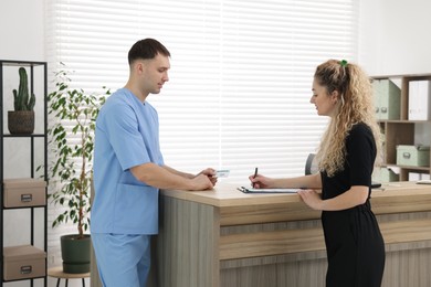 Photo of Patient filling document and receptionist with medical insurance card at counter in clinic