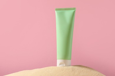 Tube of sun protection product on sand against pink background