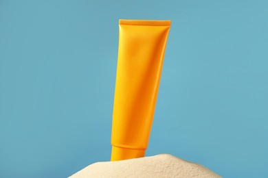 Photo of Tube of sun protection product on sand against light blue background