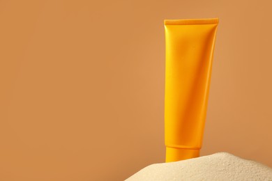 Photo of Tube of sun protection product on sand against beige background, space for text