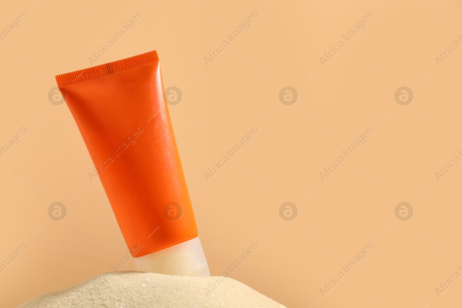 Photo of Tube of sun protection product on sand against beige background, space for text