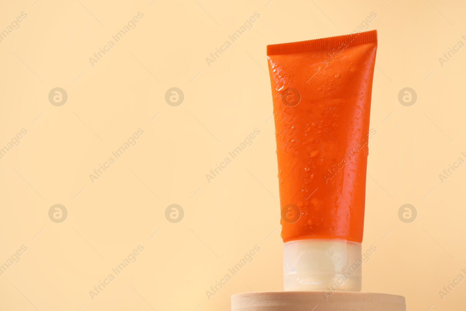 Photo of Tube of sun protection product on podium against beige background, space for text