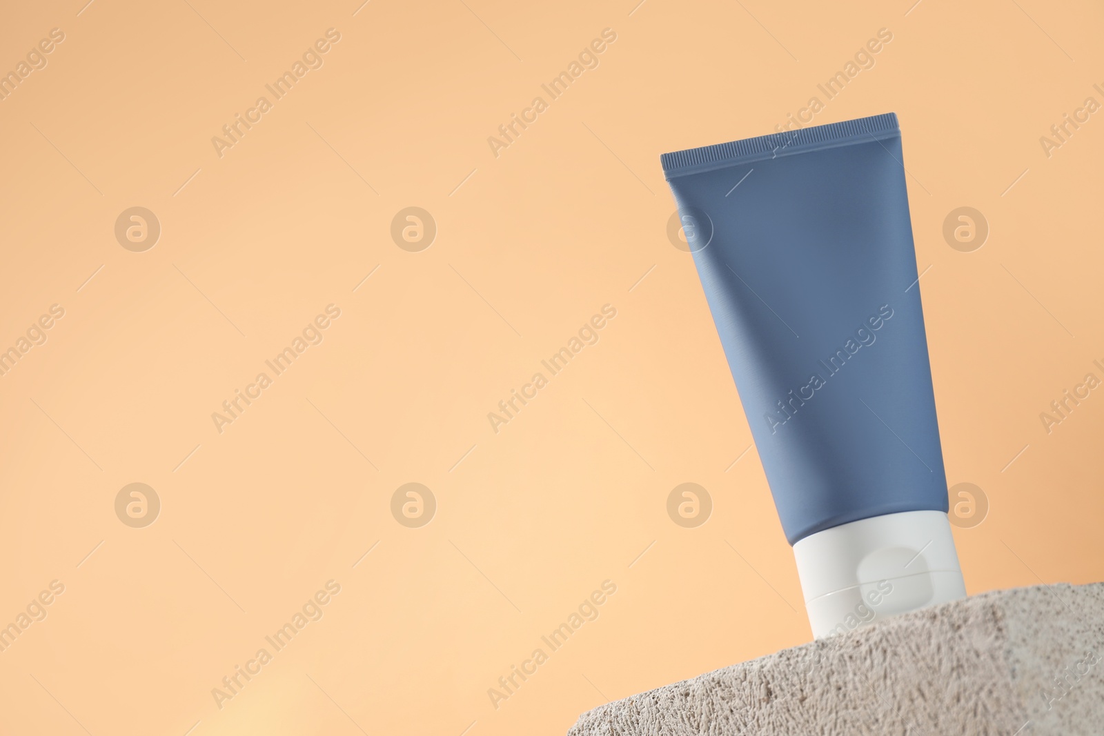 Photo of Tube of sun protection product on stone against beige background, low angle view