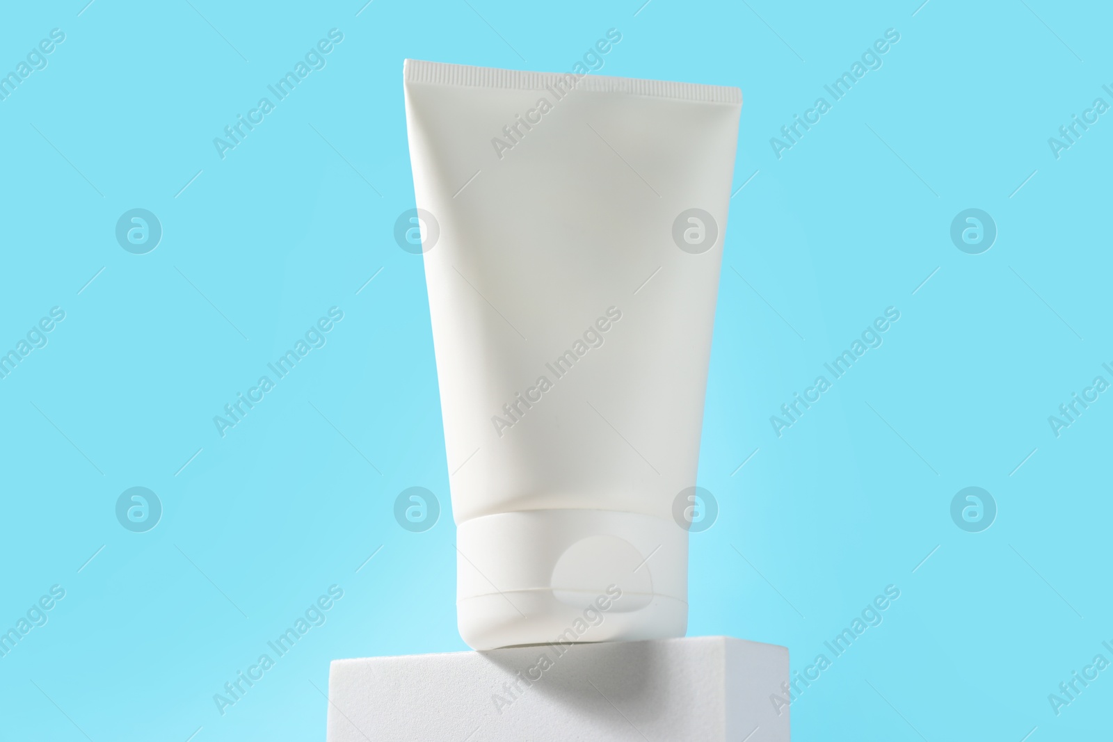 Photo of Bottle of sun protection product on podium against light blue background