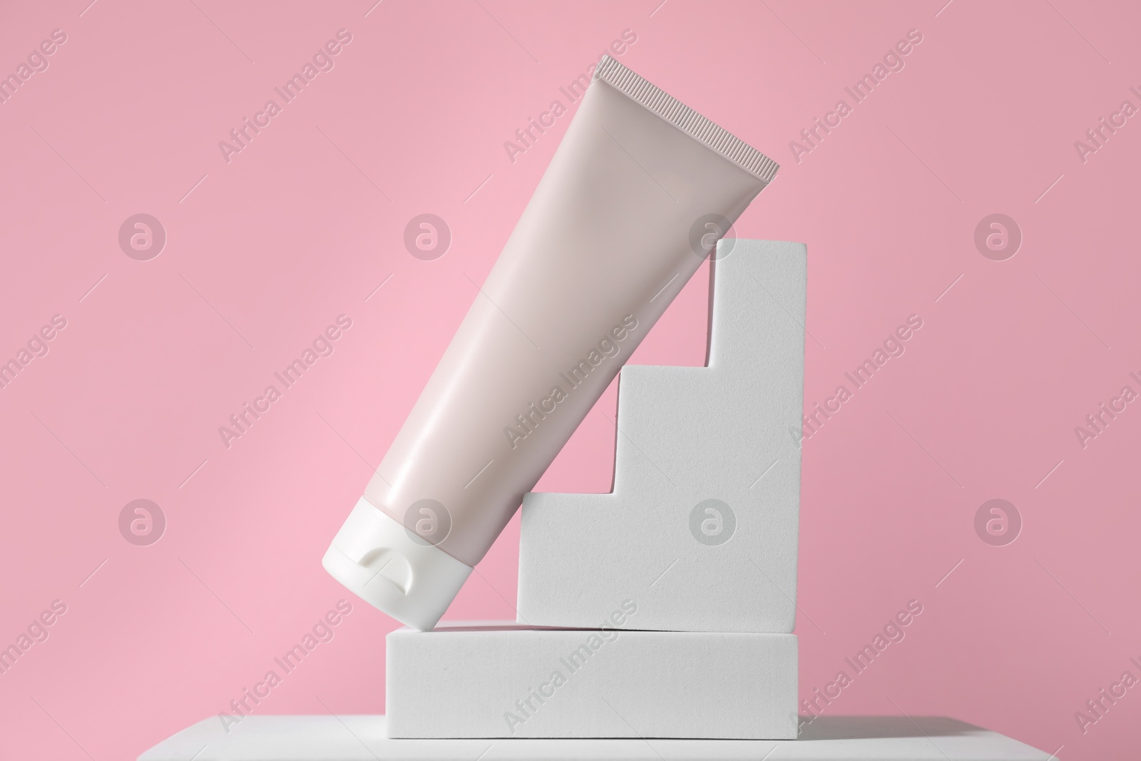 Photo of Tube of sun protection product on podium against pink background