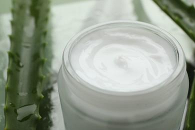 Photo of Moisturizing cream with extract of aloe vera and wet leaf on mirror surface, closeup