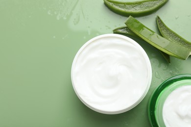 Moisturizing cream with extract of aloe vera, cut leaves and water drops on green background, flat lay. Space for text