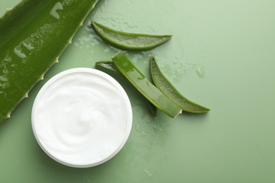 Moisturizing cream with extract of aloe vera, cut leaves and water drops on green background, flat lay. Space for text