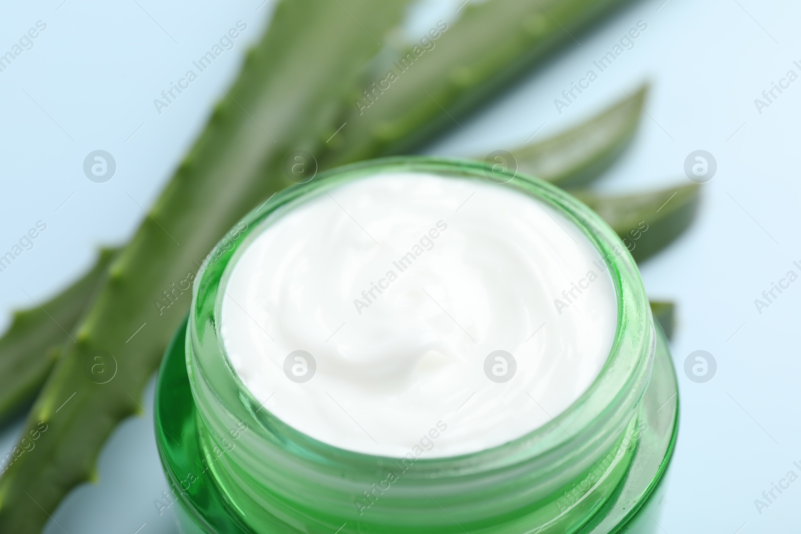 Photo of Moisturizing cream with extract of aloe vera and cut leaves on light blue background, closeup