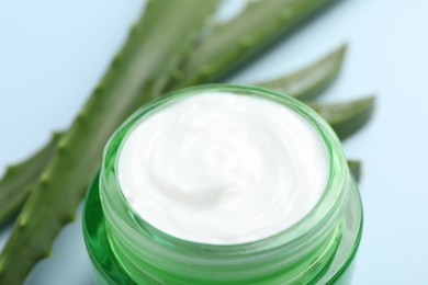 Moisturizing cream with extract of aloe vera and cut leaves on light blue background, closeup