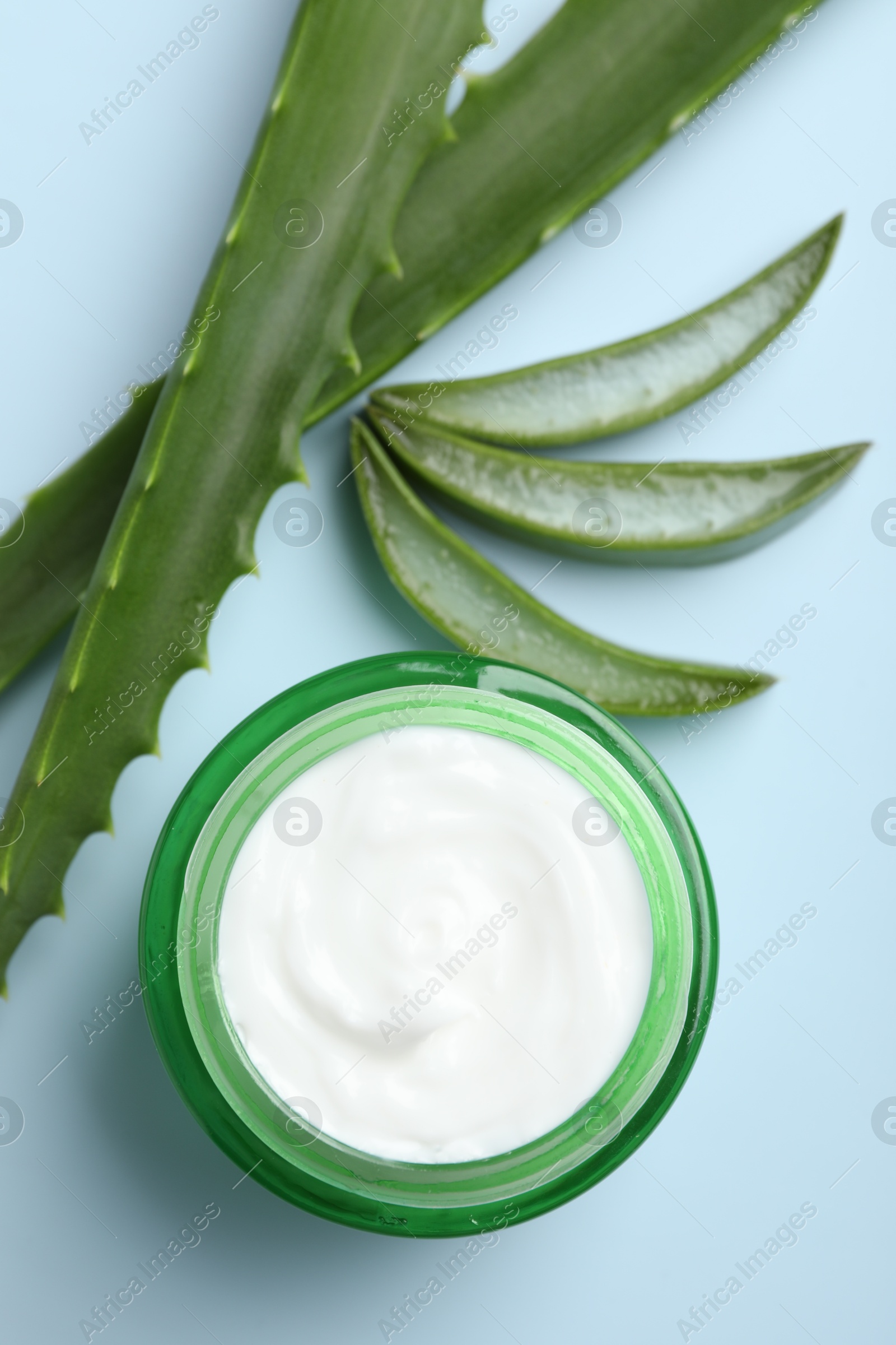 Photo of Moisturizing cream with extract of aloe vera and cut leaves on light blue background, flat lay