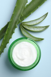 Moisturizing cream with extract of aloe vera and cut leaves on light blue background, flat lay