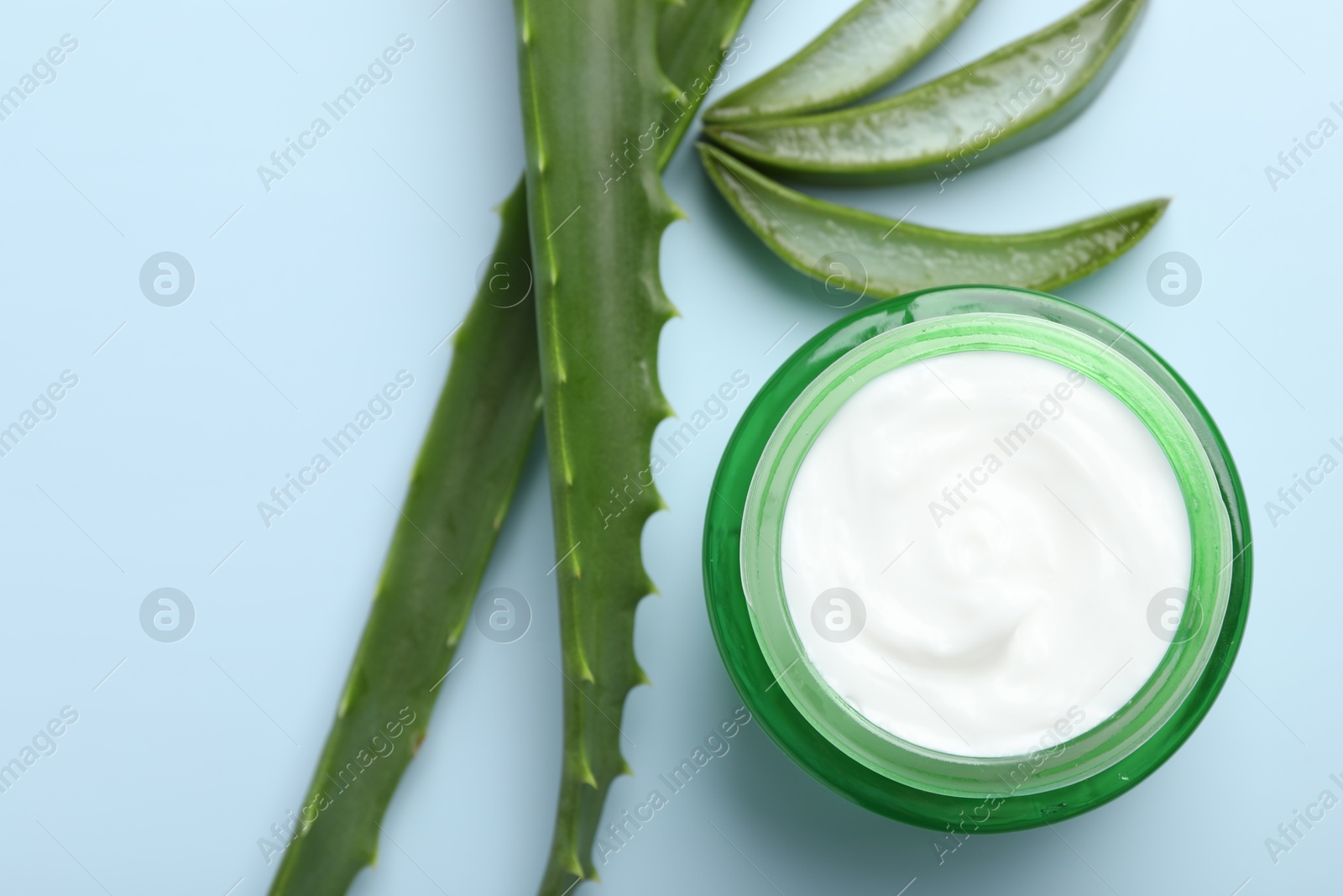 Photo of Moisturizing cream with extract of aloe vera and cut leaves on light blue background, flat lay