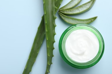 Moisturizing cream with extract of aloe vera and cut leaves on light blue background, flat lay