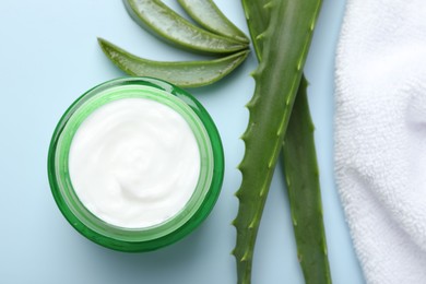 Photo of Moisturizing cream with extract of aloe vera, towel and leaves on light blue background, flat lay