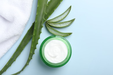 Photo of Moisturizing cream with extract of aloe vera, towel and leaves on light blue background, flat lay. Space for text