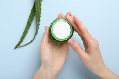 Photo of Woman with moisturizing cream and aloe vera leaves on light blue background, top view