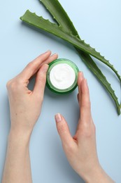 Photo of Woman with moisturizing cream and aloe vera leaves on light blue background, top view