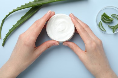 Photo of Woman with moisturizing cream and aloe vera leaves on light blue background, top view