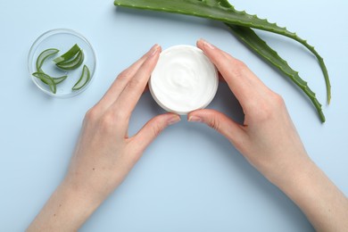 Photo of Woman with moisturizing cream and aloe vera leaves on light blue background, top view