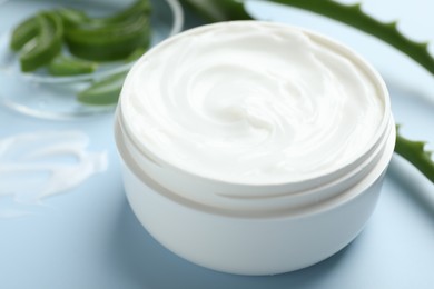 Photo of Moisturizing cream with extract of aloe vera and cut leaves on light blue background, closeup