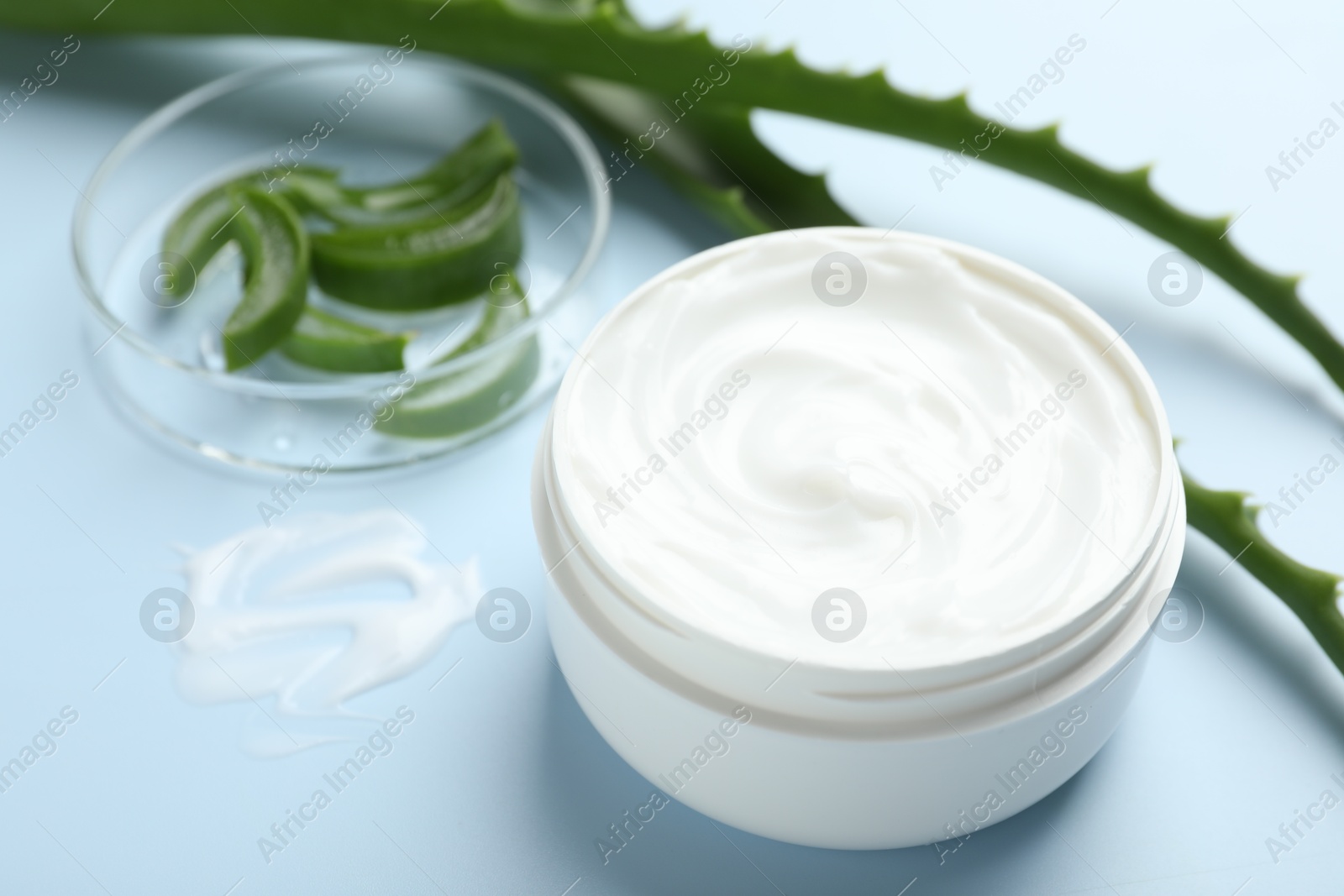 Photo of Moisturizing cream with extract of aloe vera and cut leaves on light blue background, closeup