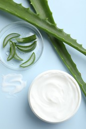 Photo of Moisturizing cream with extract of aloe vera and cut leaves on light blue background, flat lay