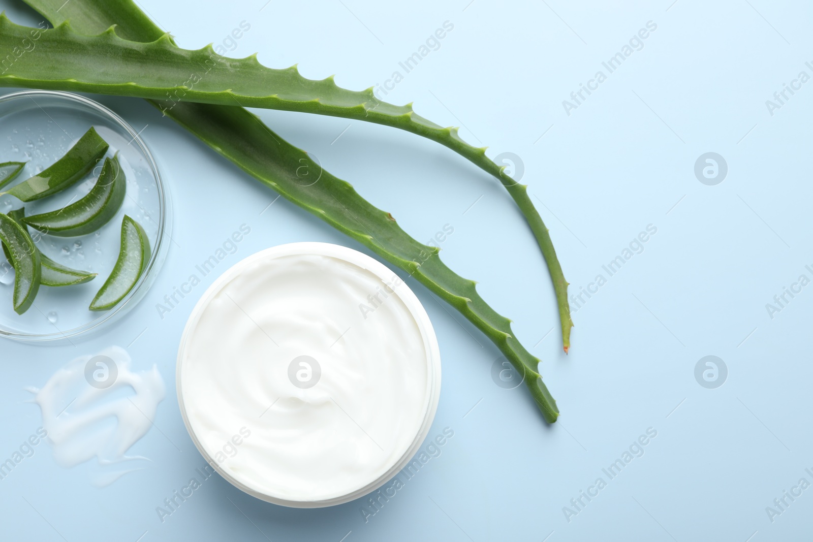 Photo of Moisturizing cream with extract of aloe vera and cut leaves on light blue background, flat lay. Space for text