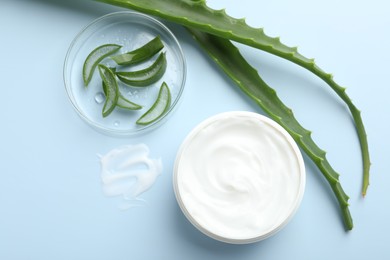 Photo of Moisturizing cream with extract of aloe vera and cut leaves on light blue background, flat lay