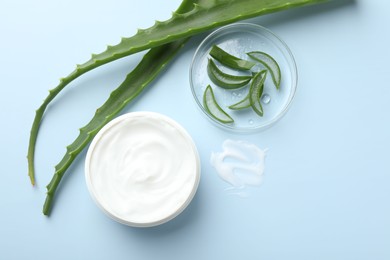 Moisturizing cream with extract of aloe vera and cut leaves on light blue background, flat lay