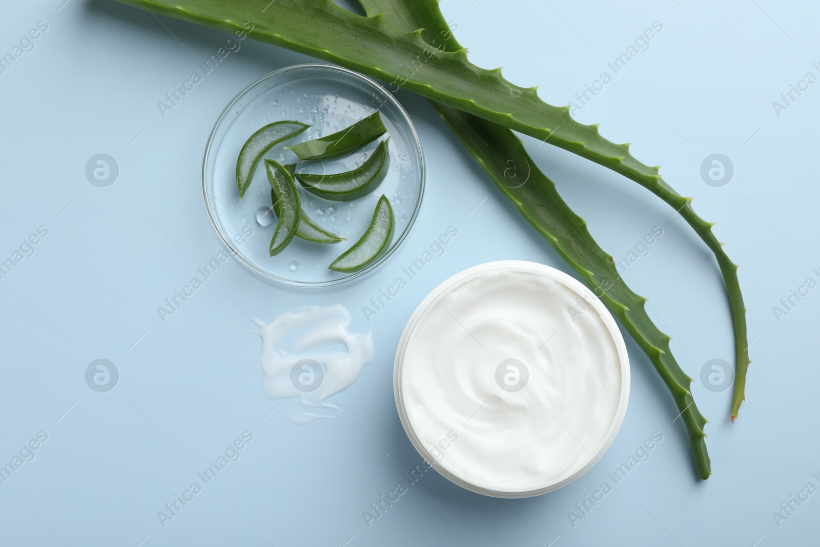 Photo of Moisturizing cream with extract of aloe vera and cut leaves on light blue background, flat lay