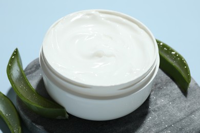 Moisturizing cream with extract of aloe vera and cut leaves on light blue background, closeup